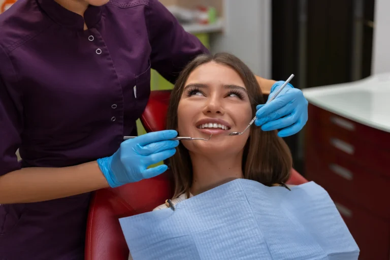 Smiling patient in a dental chair while a dental professional examines her teeth before applying dental sealants.