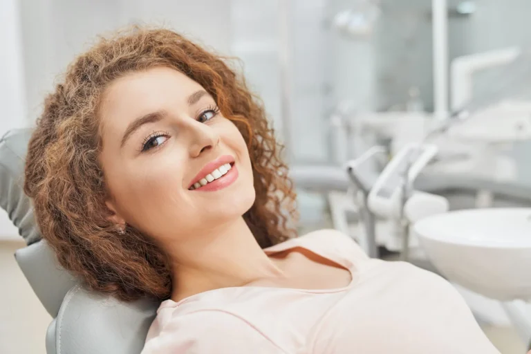 A smiling woman with curly hair lying back in a dental chair in a clinic.