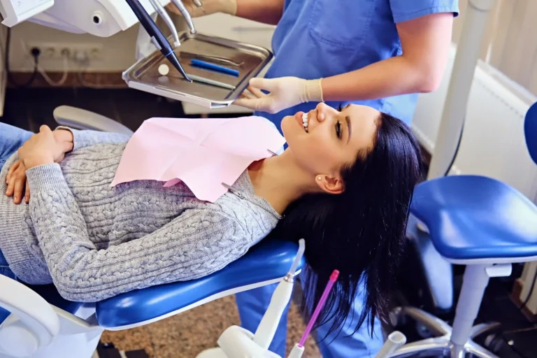 Patient smiling in a dental chair while a dental professional prepares instruments for a fluoride treatment.