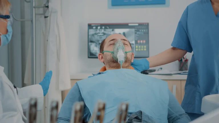 A male patient wearing an oxygen mask sits in a dental chair while receiving care from dental professionals in a clinic.