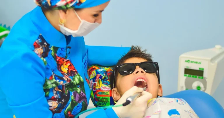 Child wearing sunglasses in a dental chair while a dental professional applies treatment to his teeth