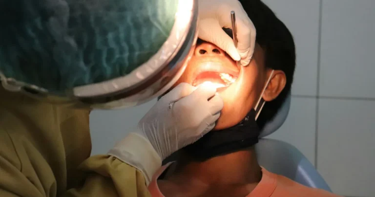 Dental professional examining a young patient's teeth under an exam light during a dental visit